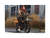 A woman wearing a black outfit with green jacket and a black bike helmet riding a green electric bike on a road in a city setting. 