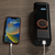 A cell phone is connected to the Rad Portable Tire Inflator and is charging via a white USB cable. 